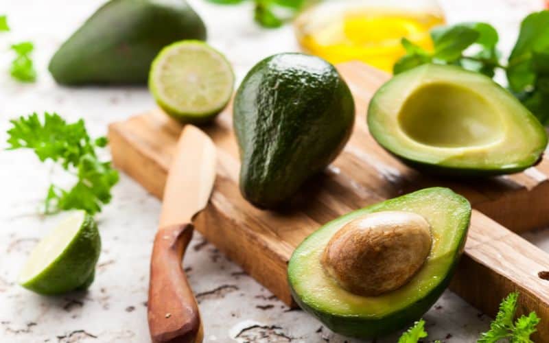 Image of a cutting board with full and halved avocado placed on it
